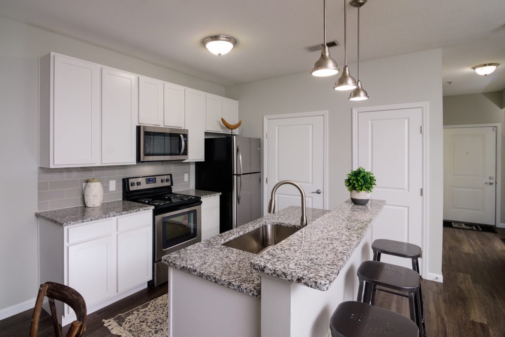 Kendall Park Kitchen with island in forefront and pendant lighting with stove and fridge in background