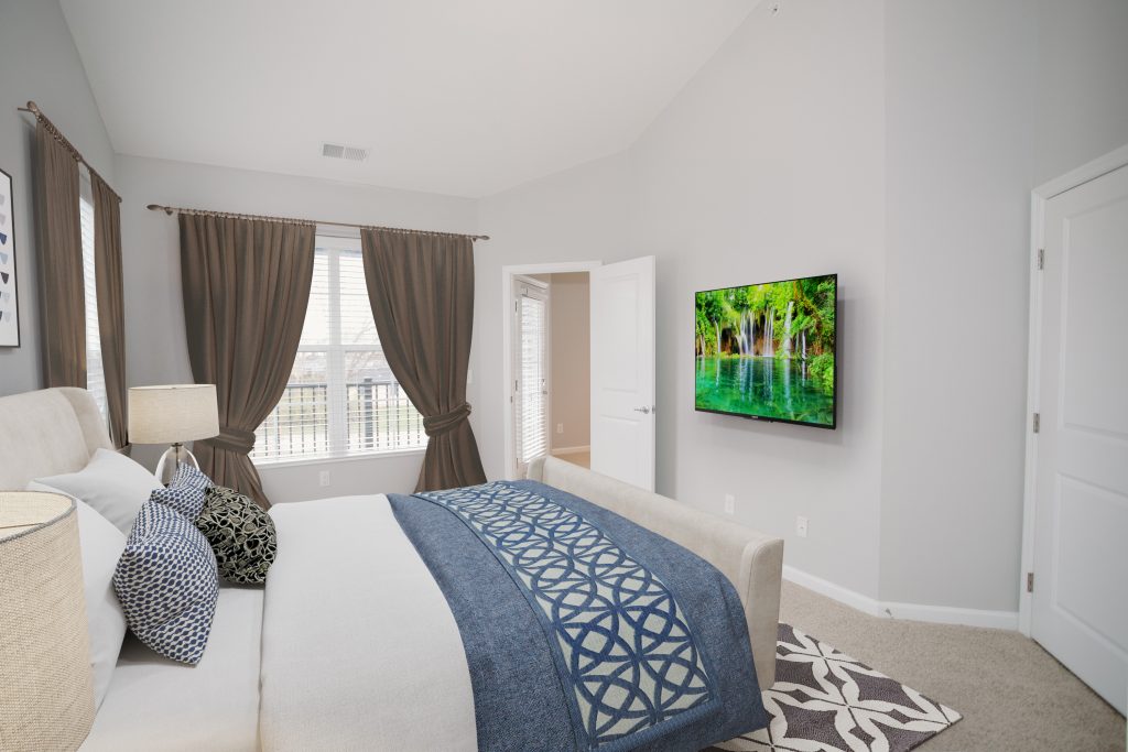 Kendall Park R Unit Master Bedroom with bed in forefront and mounted television 